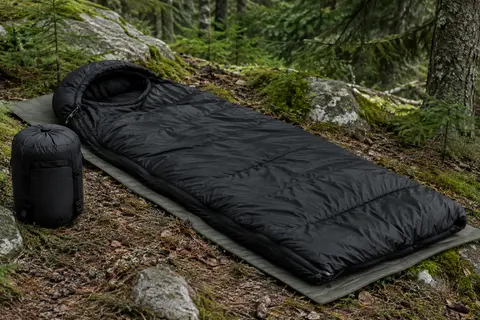 Sac de couchage rectangulaire noir avec capuche et fermeture latérale, installé dans un sous-bois