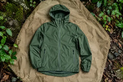 Veste imperméable baleaf pour femme posée dans un sous-bois, avec capuche et poches visibles