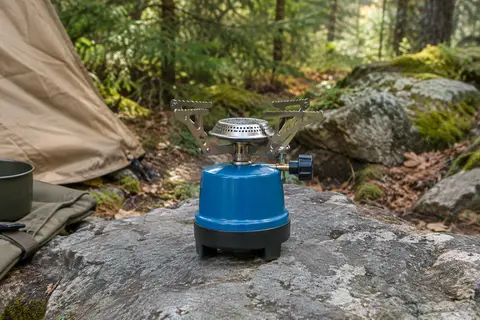 Réchaud de camping bleu à un brûleur avec supports en acier inoxydable posé dans un sous-bois