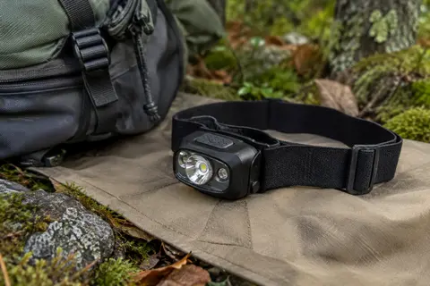 Lampe frontale noire CIRYCASE avec bandeau élastique, posée sur une toile sable en sous-bois