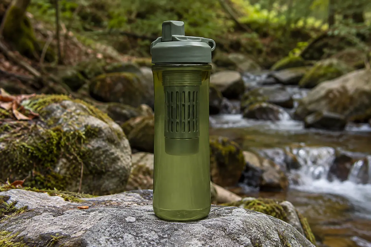 Gourde filtrante GRAYL GeoPress vert Oasis Green posée sur une pierre dans un sous-bois.