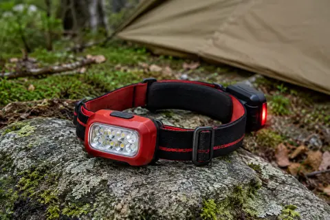 Lampe frontale rouge à huit LED posée sur une pierre dans un sous-bois calme