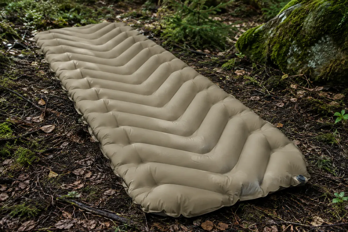 Matelas gonflable isolant sable coyote à chambres en V posé sur le sol d’un sous-bois
