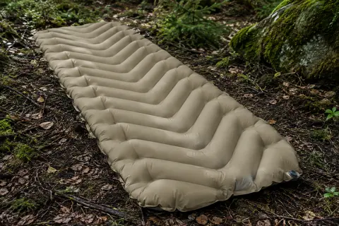 Matelas gonflable isolant sable coyote à chambres en V posé sur le sol d’un sous-bois