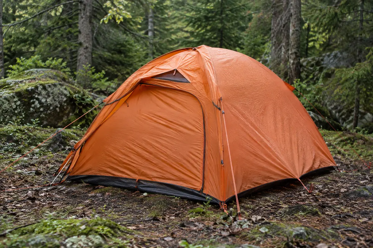 Tente dôme orange pour une personne montée dans un sous-bois, avec sa fenêtre au-dessus de la porte