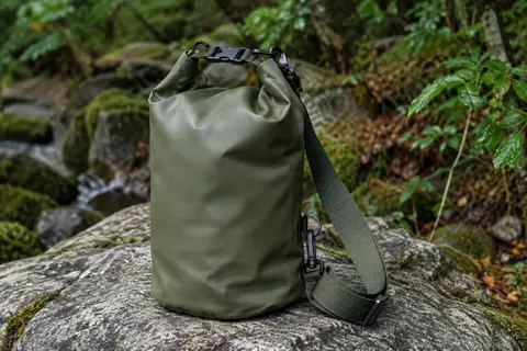 Sac étanche Nordlight vert olive en PVC, fermé par enroulement et boucle, posé en sous-bois