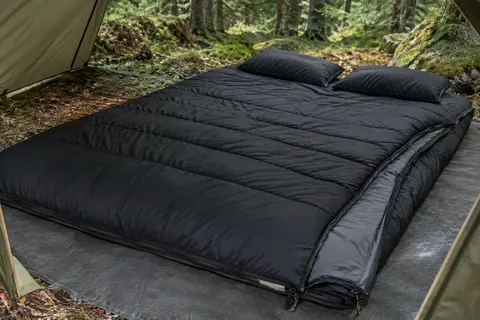 Sac de couchage double noir Ohuhu déployé avec deux oreillers dans un bivouac en sous-bois