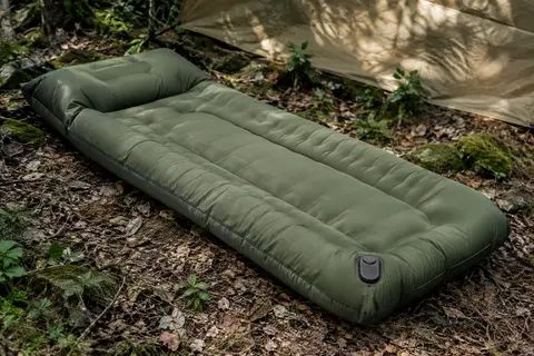 Matelas de bivouac vert militaire, épais et gonflé, posé dans un sous-bois avec son oreiller intégré.