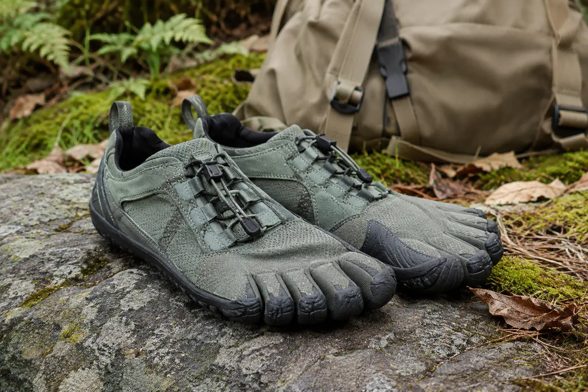 Chaussures de trail minimalistes SAGUARO à cinq doigts posées sur une pierre au bord d’un sentier forestier