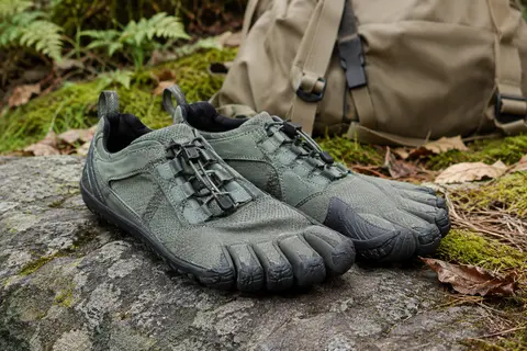 Chaussures de trail minimalistes SAGUARO à cinq doigts posées sur une pierre au bord d’un sentier forestier