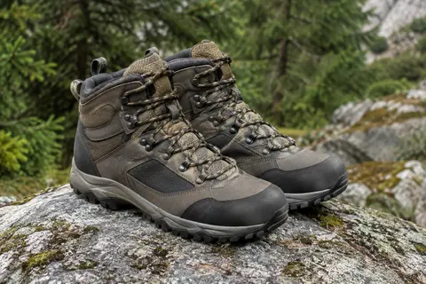 Paire de chaussures de randonnée homme mi-montantes posées sur une pierre en sous-bois