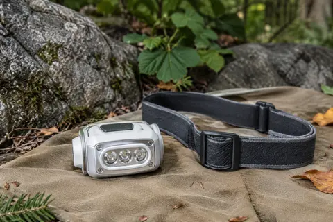 Lampe frontale blanche à trois LED avec bandeau réglable, posée sur une toile dans un sous-bois