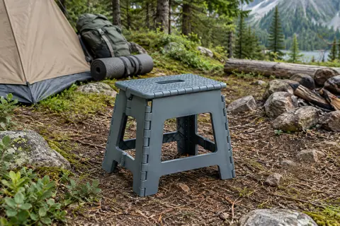 Tabouret pliant STARK gris bleu ouvert dans un sous-bois, avec sa poignée de transport intégrée
