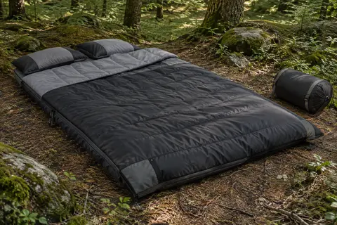 Sac de couchage double noir et gris déployé en sous-bois avec ses deux oreillers et sa housse de compression.