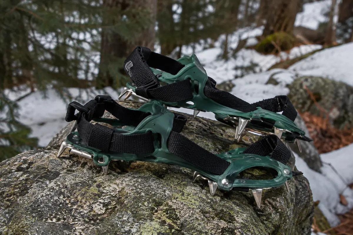 Paire de crampons Unigear verts à pointes en acier posée près d’un sentier enneigé