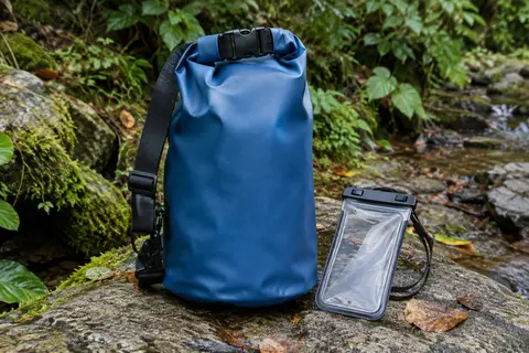 Sac étanche bleu en PVC avec fermeture roulée, sangle ajustable et pochette téléphone sur une pierre en sous-bois
