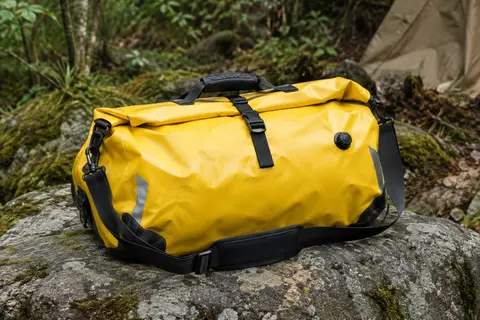 Sac étanche jaune Wild Heart de 40 litres avec fermeture roulée, posé sur une roche en sous-bois